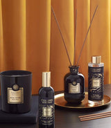 Collines de Provence Duftkollektion mit Duftkerze Schwarze Rose, Raumspray Ebenholz, Duftdiffuser Ebenholz und Duftdiffuser-Nachfüllung auf goldenem Tablett vor goldfarbenem Vorhang.