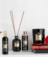 Collines de Provence Duftkollektion mit Raumspray Ebenholz, Duftdiffuser Ebenholz, Duftdiffuser-Nachfüllung Schwarze Rose und Duftkerze Zeder auf Büchern vor hellem Hintergrund