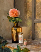 Collines de Provence Raumspray Antike Rose neben einem Duftöl und einer rosa Rose in einer braunen Glasvase