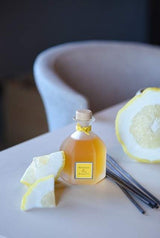 Collines de Provence Duftdiffuser Mandarine & Yuzu mit dekorativem Glasflakon auf einem Tisch, arrangiert mit Zitrusschalen und Duftstäbchen.