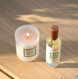 Collines de Provence Duftkerze Aloe Vera und Raumspray Aloe Vera auf einer Holzoberfläche mit brennender Kerze im Sonnenlicht.