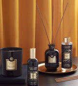 Collines de Provence Duftkollektion mit Duftkerze Schwarze Rose, Raumspray Ebenholz, Duftdiffuser Ebenholz und Duftdiffuser-Nachfüllung Ebenholz auf goldenem Tablett vor goldfarbenem Vorhang.