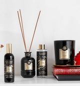 Collines de Provence Duftkollektion mit Raumspray Ebenholz, Duftdiffuser Ebenholz, Duftdiffuser-Nachfüllung Schwarze Rose und Duftkerze Zeder auf Büchern vor hellem Hintergrund.