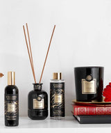 Collines de Provence Duftkollektion mit Raumspray Ebenholz, Duftdiffuser Ebenholz, Duftdiffuser-Nachfüllung Schwarze Rose und Duftkerze Zeder auf Büchern vor hellem Hintergrund.