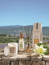 Collines de Provence Duftset mit Duftkerze Mandelblüte, Raumspray Weiße Lilie und Duftdiffusor Weiße Lilie auf Naturstein vor Lavendellandschaft.