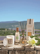 Collines de Provence Duftset mit Duftkerze Mandelblüte, Raumspray Weiße Lilie und Duftdiffusor Weiße Lilie auf Naturstein vor Lavendellandschaft.