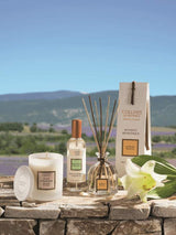 Collines de Provence Duftset mit Duftkerze Mandelblüte, Raumspray Weiße Lilie und Duftdiffusor Weiße Lilie auf Naturstein vor Lavendellandschaft.