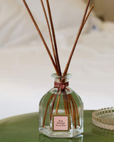 Collines de Provence Raumduft Diffuser Antike Rose im Glasflakon mit braunen Duftstäbchen auf grünem Beistelltisch