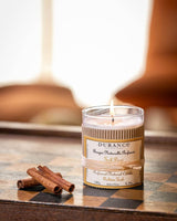 Durance Duftkerze Golden Teak brennend auf dekorativem Holztisch mit Zimtstangen im gemütlichen Wohnzimmer