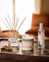 Durance Raumspray Golden Teak Glasflasche mit silbernem Sprühkopf neben Duftkerze und Diffuser auf Holztisch