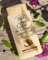 Le Petit Olivier Creme-Shampoo mit Olivenöl, Sheabutter und Arganöl auf Holzuntergrund mit grünen Blättern und violetten Blüten