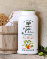 Le Petit Olivier Duschcreme Orangenblüte neben einem Holzeimer mit Naturschwamm und Handtuch