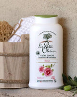 Le Petit Olivier Duschcreme Rose neben einem Holzeimer mit Naturschwamm und Handtuch