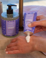 Anwendung der Panier des Sens Handcreme Lavendel aus der Provence 75ml. Eine Person trägt die reichhaltige Handcreme auf den Handrücken auf. Im Hintergrund stehen passende Pflegeprodukte der Lavendel-Serie. 